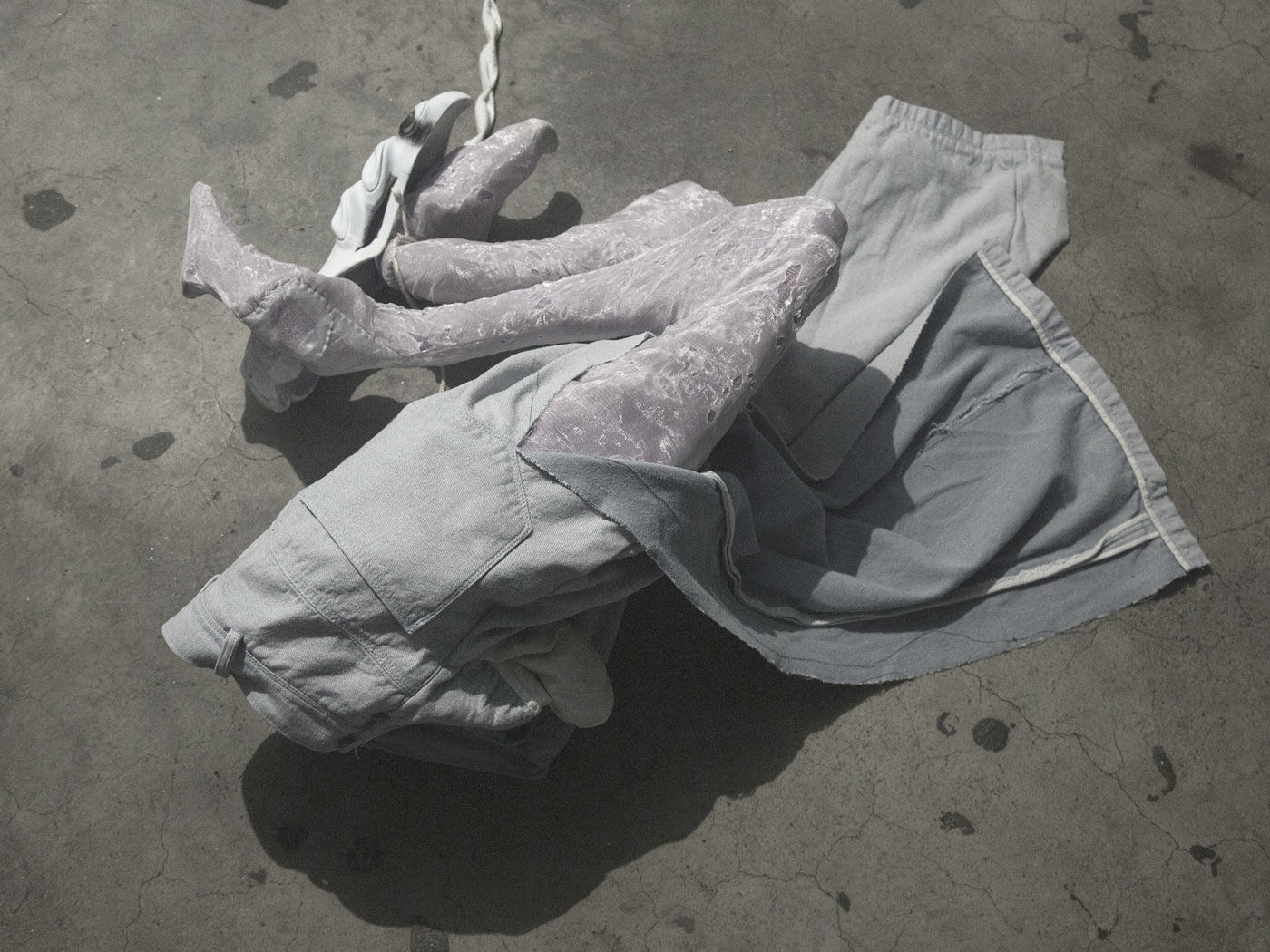 A crouched lower body. The trousers are torn along the center back, exposing the legs. The legs are cramped and made of perforated laserscrim material.