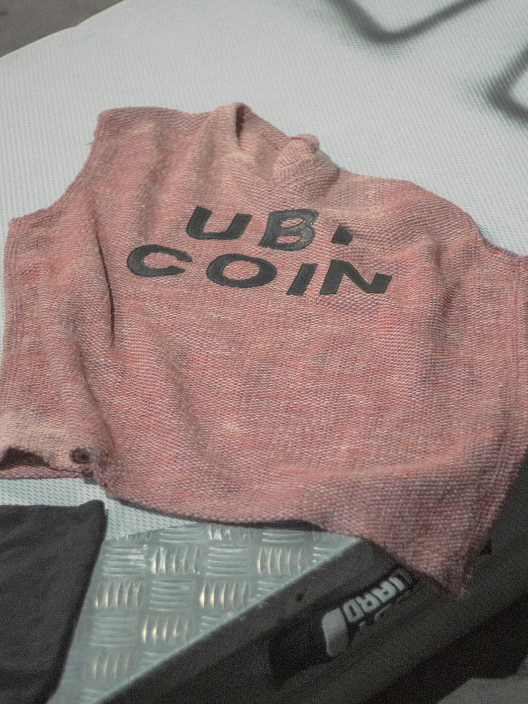 A top made of rose-colored costume fabric on a light grey mattress. The lettering Ub1 Coin can be read on the top.