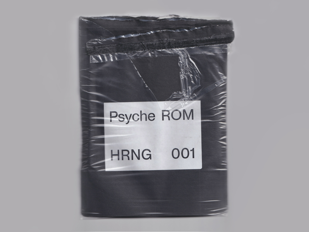 A torn open, cellophane-wrapped black zip bag. There is a white sticker on the pouch which reads Psyche ROM HRNG 001 in a sans serif font.